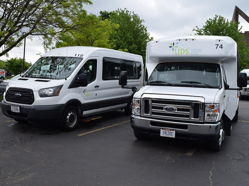 Two white UDS transportation vans are parked in a parking lot.