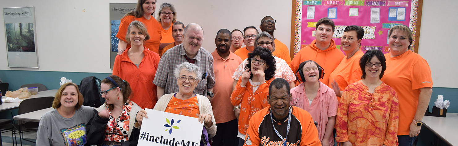 A diverse group of adults of varying races and abilities smile for the camera at UDS. They wear orange to represent inclusion.