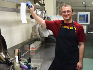 a male kitchen worker for Taste Buds smiles int he kitchen prep area