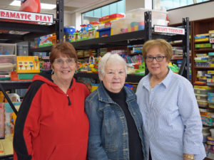Three volunteers smile for the camera in the Toy and Resource Center at UDS